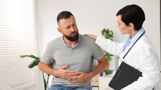 Male patient holding his abdomen while talking with a doctor, illustrating discussion about frequent nighttime urination or nocturia causes.
